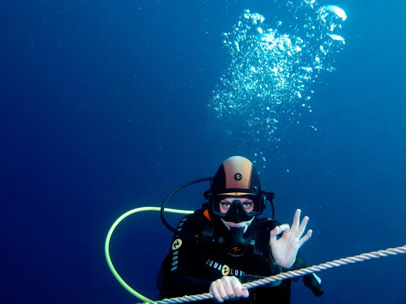 Plongeur en combinaison noire fait le signe OK sous l'eau