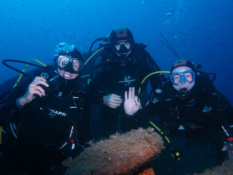 Trois plongeurs souriants, équipés, posent devant la caméra sous-marine