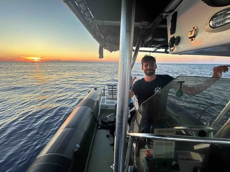 Homme souriant sur un bateau semi-rigide en mer au coucher du soleil