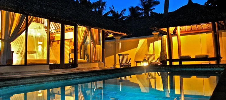 Bâtiment éclairé avec piscine reflétant la lumière, ambiance tropicale calme
