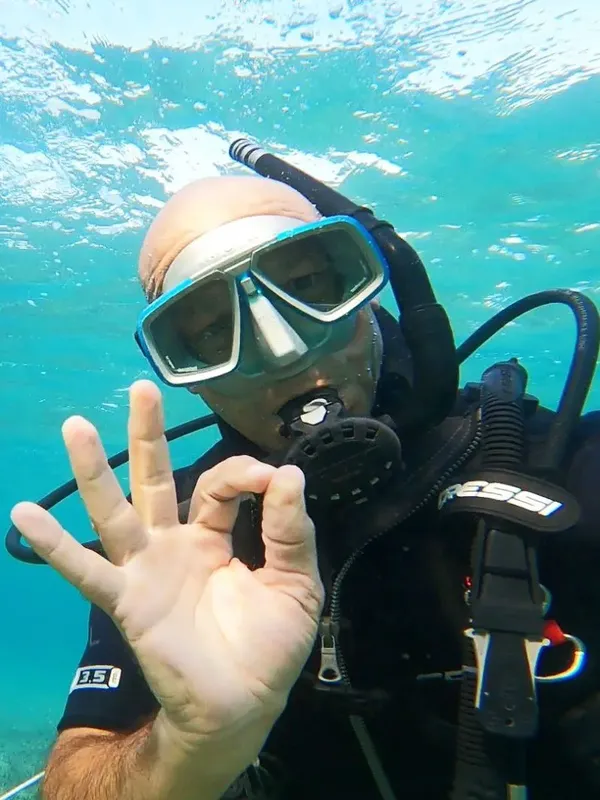 Plongeur souriant avec signe OK, eau turquoise, équipement complet