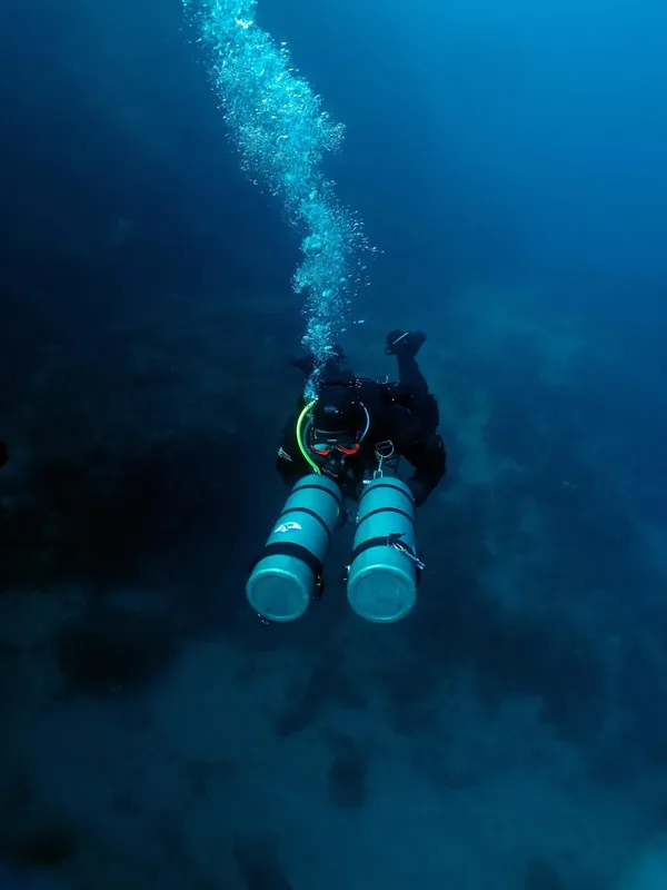 Plongeur en scaphandre noir évolue dans une eau bleue profonde