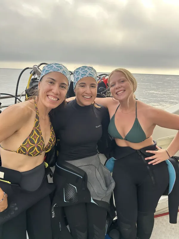 Trois plongeuses souriantes sur un bateau, équipées pour une sortie