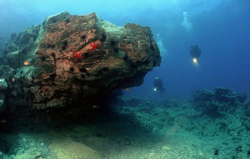 Deux plongeurs explorent un récif rocheux sous l'eau en bleu profond