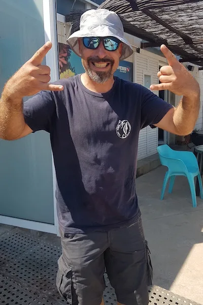Homme souriant avec chapeau et lunettes de soleil fait le signe shaka