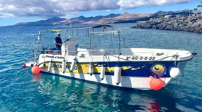 Bateau de plongée jaune et blanc amarré en mer avec un homme à bord