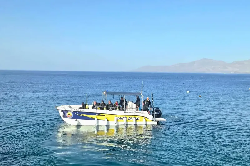 Bateau de plongée avec des plongeurs en mer, ciel bleu et montagnes