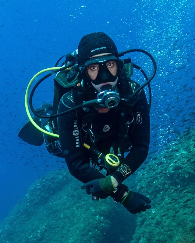 Plongeur en combinaison regarde la caméra dans l'eau bleue