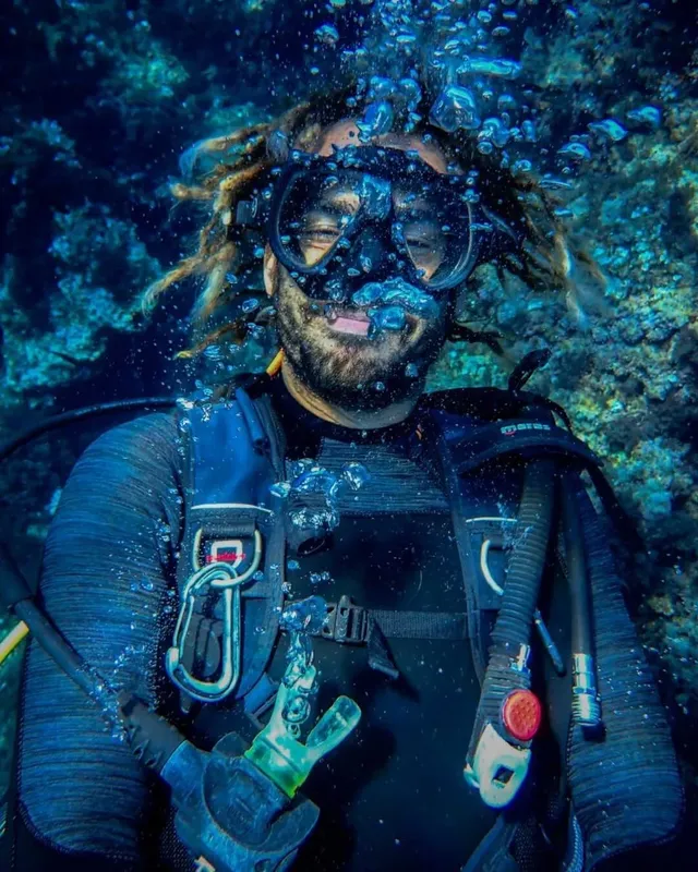 Plongeur souriant avec des dreadlocks, entouré de bulles sous-marines