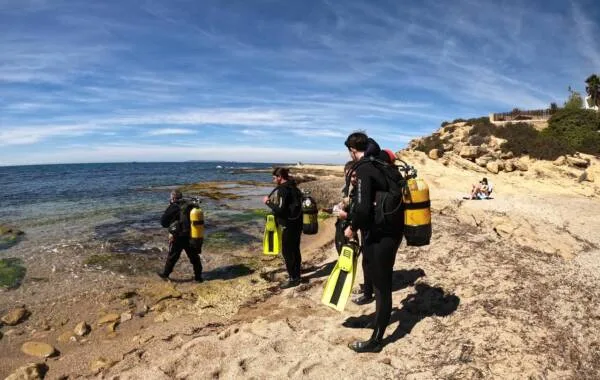 Plongeurs équipés se préparent sur une plage rocheuse ensoleillée