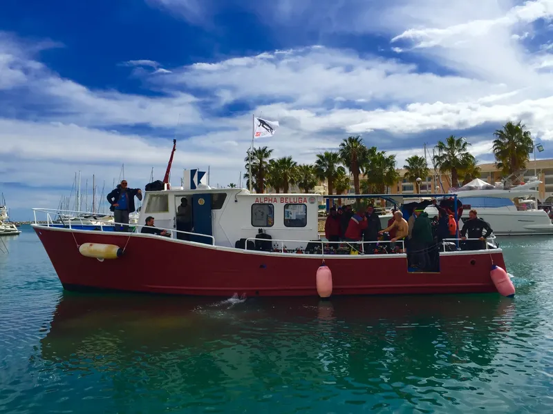 Bateau de plongée rouge amarré dans un port ensoleillé avec des plongeurs
