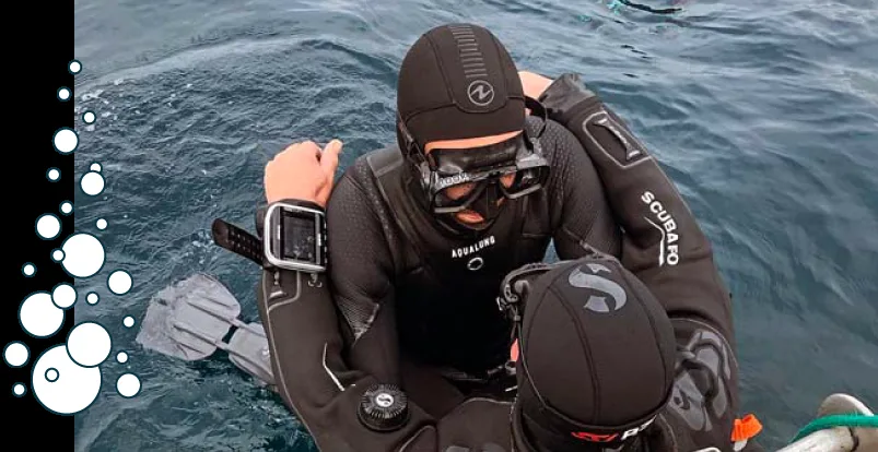 Deux plongeurs en combinaison, un montre son ordinateur de plongée