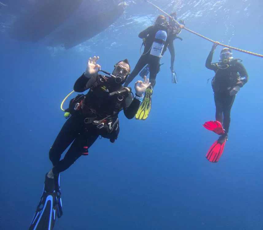 Trois plongeurs souriants font des signes de paix sous l'eau