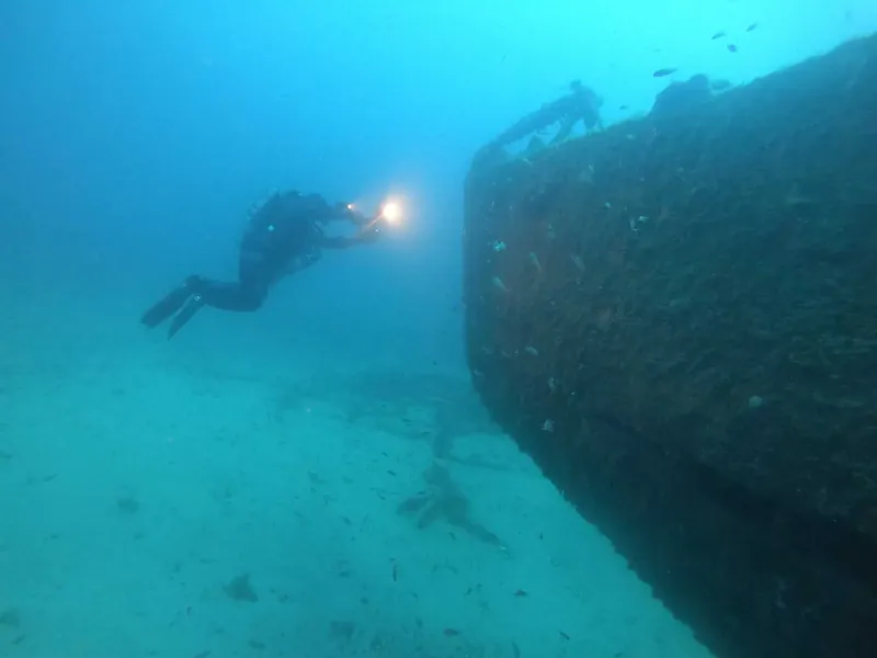 Plongeur explorant l'épave d'un navire sous l'eau avec une lampe