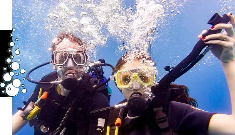 Deux plongeurs souriants avec leur équipement, bulles et eau bleue