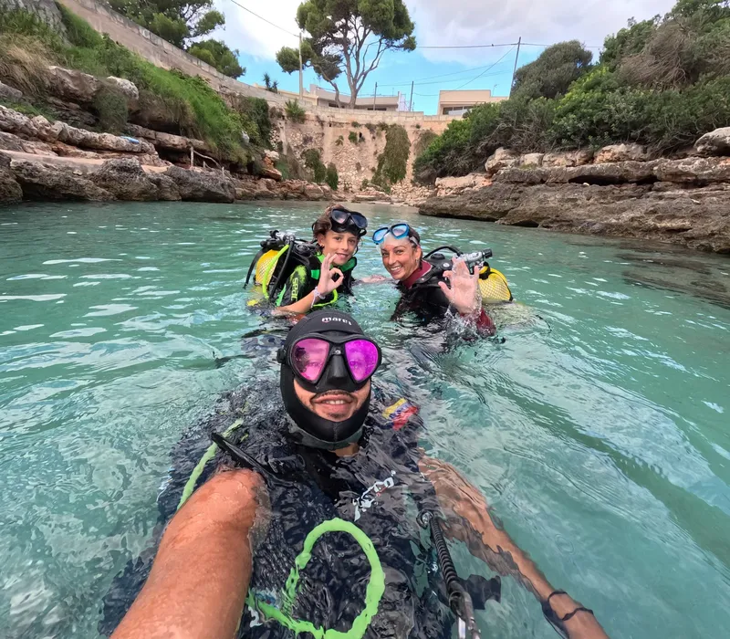 Trois plongeurs souriants en combinaison et masque dans une eau turquoise