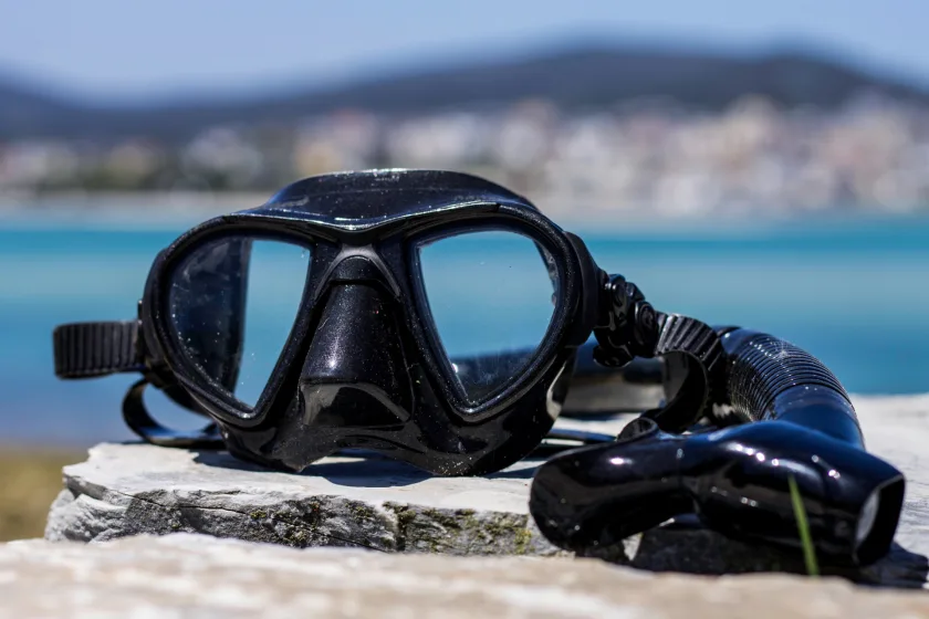 Masque de plongée noir et tuba sur un mur de pierre, mer en arrière-plan