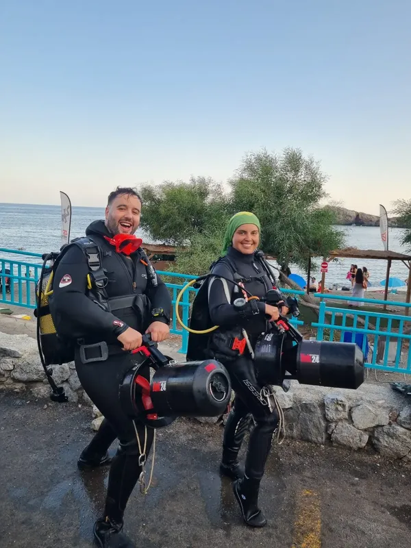 Deux plongeurs souriants équipés près d'une plage ensoleillée