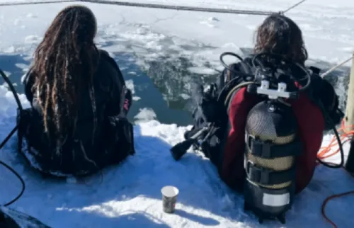 Deux plongeurs assis sur la glace, équipés, préparent leur matériel