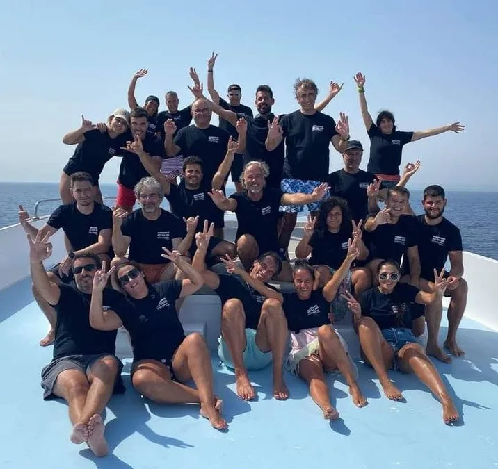Groupe de personnes souriantes sur un bateau en mer, signe de la paix