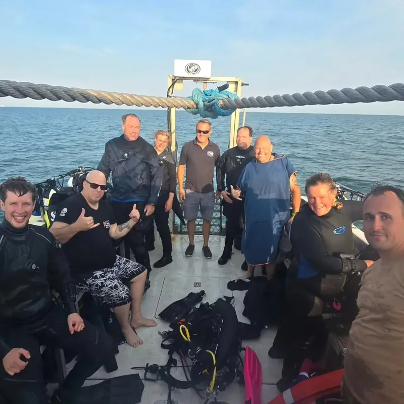 Groupe de plongeurs souriants sur un bateau en mer, équipement visible