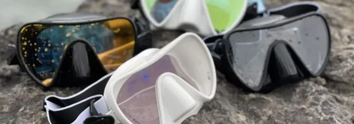 Plusieurs masques de plongée de différentes couleurs sont présentés sur un sol rocheux