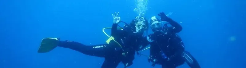 Deux plongeurs souriants font des signes de la main sous l'eau