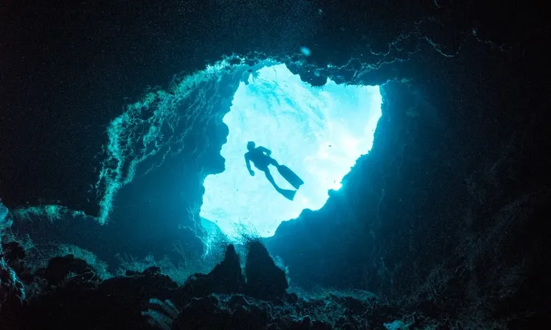 Plongeur silhouette sombre explorant une grotte sous-marine éclairée par le soleil