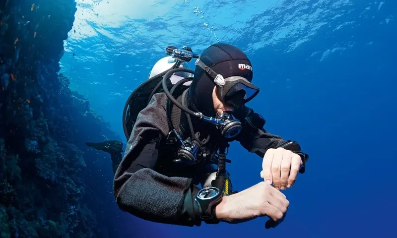 Plongeur en combinaison regarde sa montre sous l'eau en mer