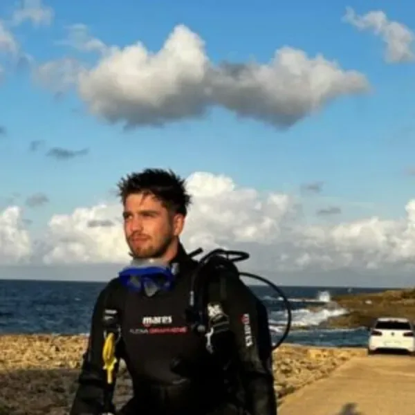 Plongeur en combinaison regarde au loin, mer et voiture en arrière-plan