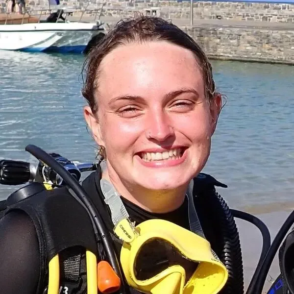 Plongeuse souriante avec masque et gilet, devant des bateaux amarrés