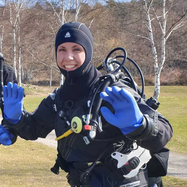 Plongeuse souriante en équipement complet, gants bleus, sur fond flou