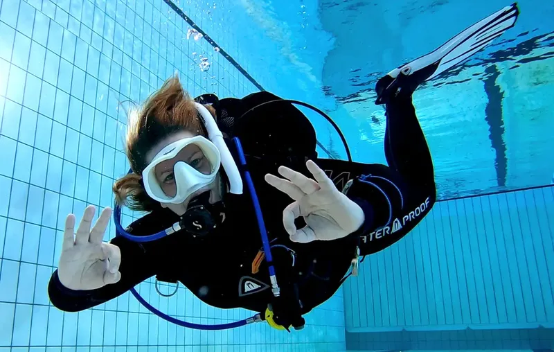 Plongeuse souriante en combinaison, masque et palmes, geste OK, piscine
