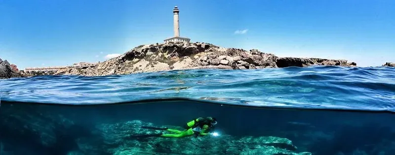 Plongeur explorant un récif rocheux avec un phare en arrière-plan
