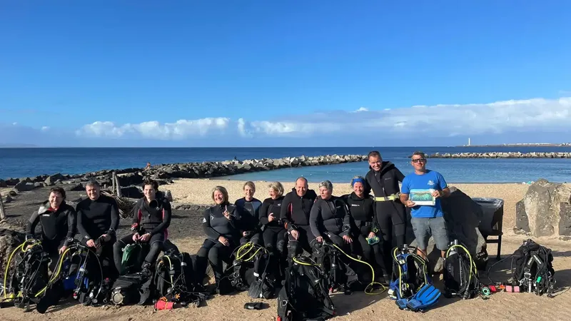 Groupe de plongeurs souriants équipés sur une plage ensoleillée