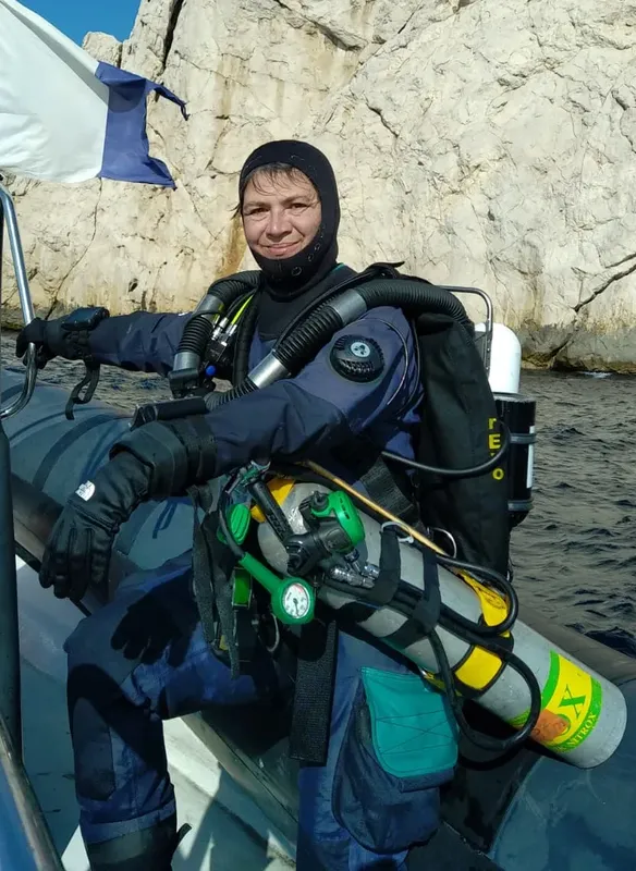 Plongeuse souriante en combinaison complète, prête à plonger depuis un bateau