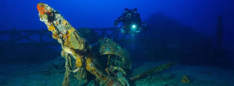 Plongeur explorant une épave métallique recouverte d'algues en profondeur