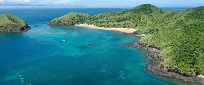 Cote rocheuse verte, plage de sable, mer turquoise et petit bateau