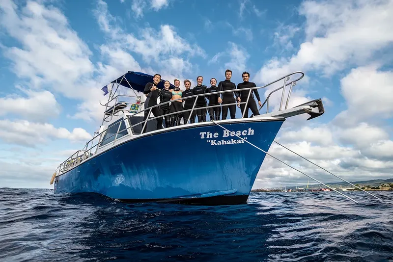 Groupe de plongeurs souriants sur la proue d'un bateau bleu en mer