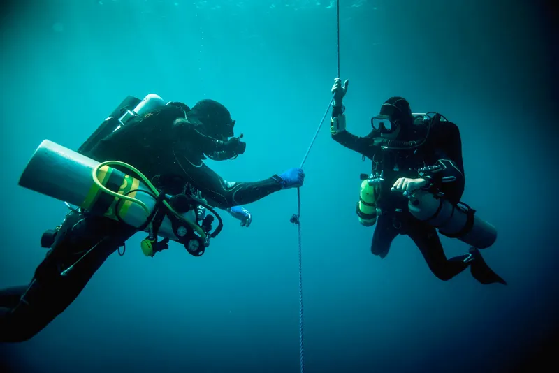 Deux plongeurs en combinaison s'entraident sous l'eau avec une corde