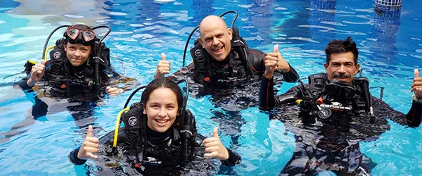 Trois plongeurs souriants avec leur équipement complet dans l'eau