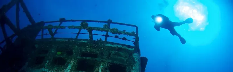 Plongeur explore une épave métallique recouverte d'algues en bleu