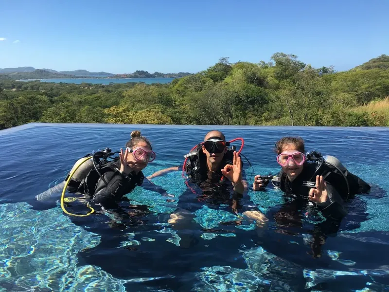 Trois plongeurs souriants en équipement complet dans une piscine à débordement