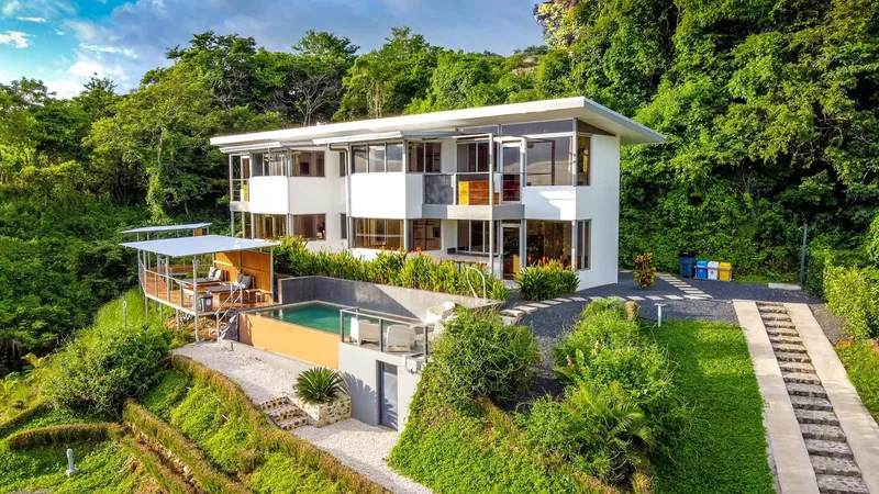 Bâtiment moderne blanc avec piscine, végétation luxuriante et allée pavée