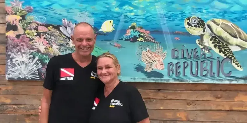 Un couple souriant pose devant une fresque marine colorée