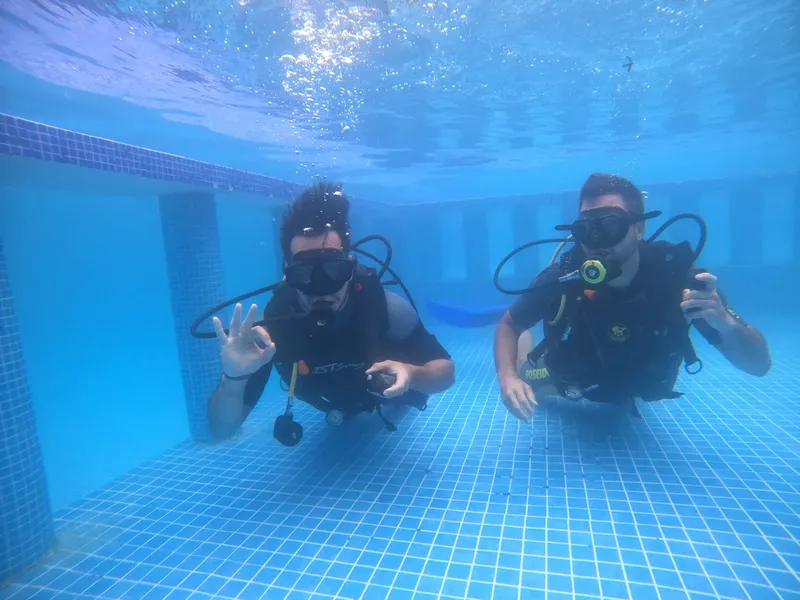 Deux plongeurs en formation dans une piscine, sourires et signes de la main