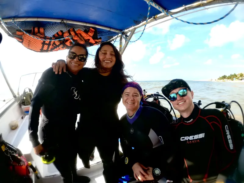 Quatre plongeurs souriants sur un bateau en mer, équipés et prêts