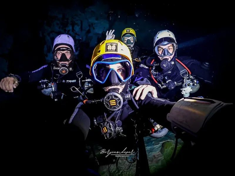 Quatre plongeurs souriants posent ensemble dans l'obscurité sous-marine