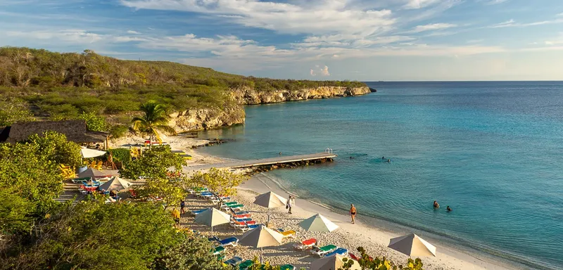Plage de sable blanc avec transats, personnes se baignant et ponton