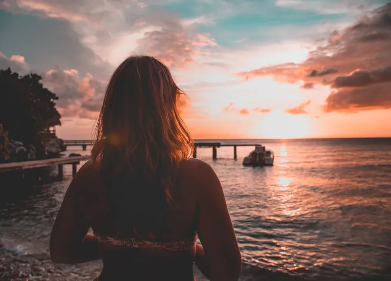 Dos d'une personne regardant un bateau au coucher du soleil